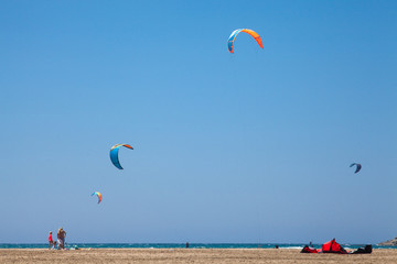People practicing Kitesurfing. Beach on the peninsula Prasonisi, Rhodes. Colorful kites on the sea shore. Blue sea and windsurfing.