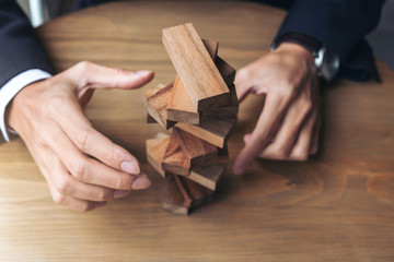 Fototapeta na wymiar Alternative risk concept, plan and strategy in business, Young intelligent businessman raise the wood game, hands of executive sustain wood block on the tower, Collaborative management