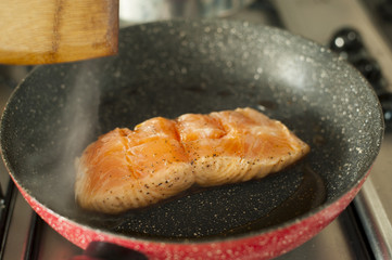 A piece of salmon fillet sizzling in a hot pan.