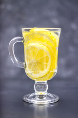 Homemade lemonade in a glass with a handle on a gray concrete background. Water with slices of lemon on a dark background.