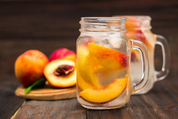 Mason jar glass of homemade peach iced water on a rustic wooden background.