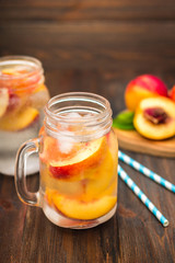 Mason jar glass of homemade peach iced water on a rustic wooden background.