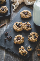 Obraz na płótnie Canvas Homemade oatmeal raisin cookies with chocolate and milk on slate background. Selective focus, toned image