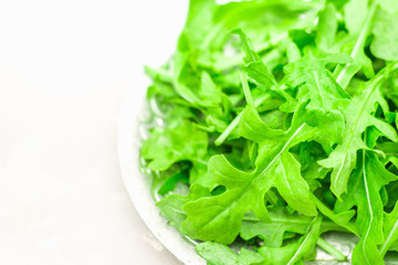 Fresh juicy leaves of arugula on a light concrete background.