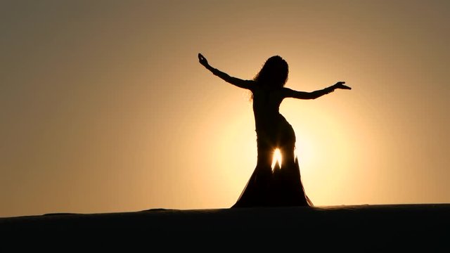 Girl cute performs beautiful belly dance on sunset background. Silhouette