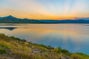 Dramatic view and magic sunbeam at sunset, mountain background. Tranquil panorama landscape of Yang Choom Reservoir, Kui Buri, Prachuap Khirikhan, Thailand.