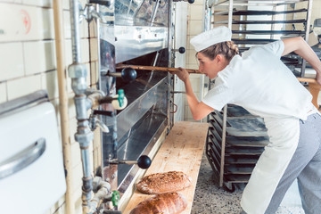 Bäcker Frau holt frisch gebackenes Brot aus dem Ofen in ihrer Bäckerei