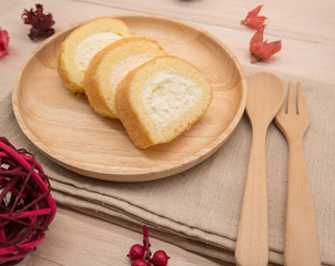 Obraz na płótnie Canvas Cake roll in wooden dish with wooden spoon and fork on beige wooden table,background and copy space