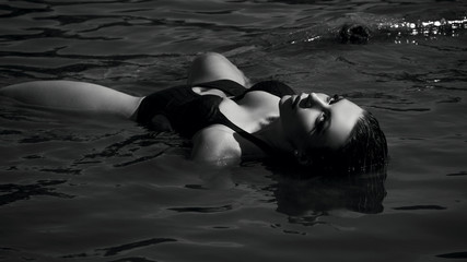 A coveted sexy girl or woman in erotic lingerie seductively lies in the water spreading her legs. black and white photo