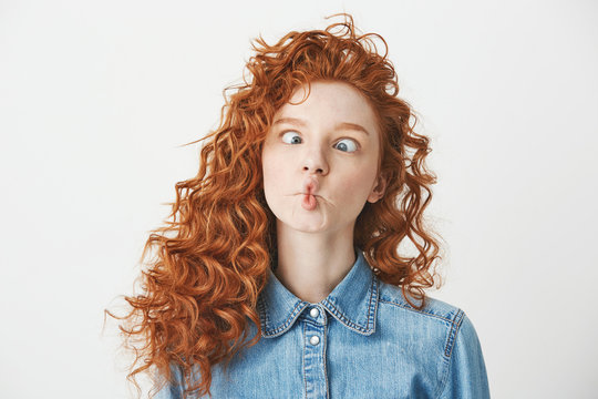 Cute young girl with foxy curly hair making funny face over white background. Copy space.