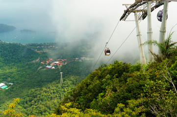 Fototapeta premium Cable car tower fixed atop a hill with the cable and cablecars going down. The sea is visible in the distance with cloudy skies and fog