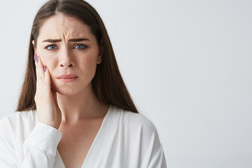 Fototapeta premium Sad upset young girl looking at camera with hand on face over white background.