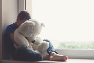 Sad child sitting on window