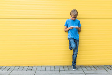 Child with mobile phone standing near yellow wall outside