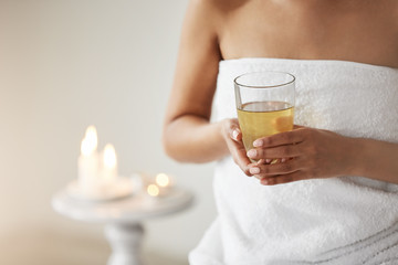 Close up of young girl in towel holding glass with green tea in spa salon.