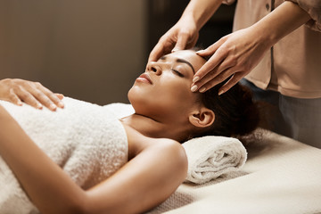 Obraz na płótnie Canvas Attractive african girl enjoying face massage in spa salon.