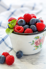 Ripe raspberries and blueberries in an enamel mug.