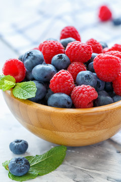 Ripe raspberries and blueberries in a wooden bowl.