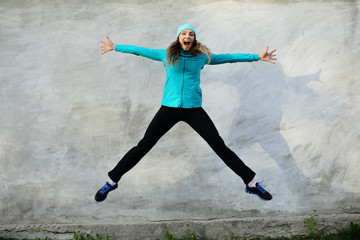 Sport healthy jump, gray wall, woman jumping sport outdoor, street, looking camera