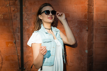 Fototapeta premium Stylish summer young woman in beautiful sunglasses, standing on brick background, looking camera