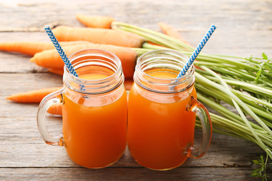 Fresh carrot juice in glass jars on grey wooden background