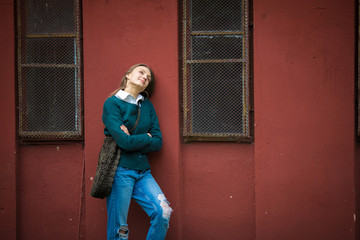 Enjoying resting woman standing near red metallic wall, urban background