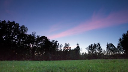 After sunset sky over meadow and forest
