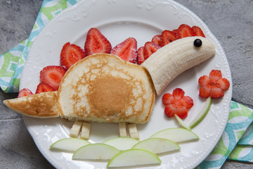 Funny dinosaur shaped pancake with strawberry, banana and chocolate