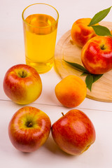 Glass of juice and ripe apples and peaches on a wooden table