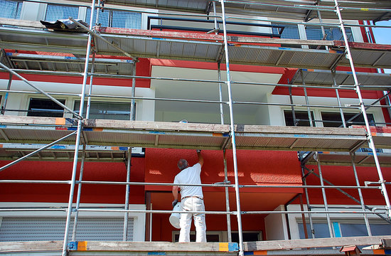 Maler auf Gerüst streicht die Außenfassade eines Mehrfamilienhauses