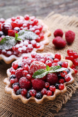 Dessert tartlets with berries and powdered sugar on grey wooden table