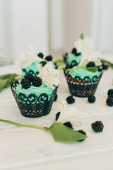 Delicate tasty muffins with mint cream decorated with fresh blackberries and orchid flowers on a wooden background.