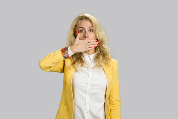 Portrait of shocked woman covering mouth. Surprised young woman covering her mouth with her hand, isolated on grey background.