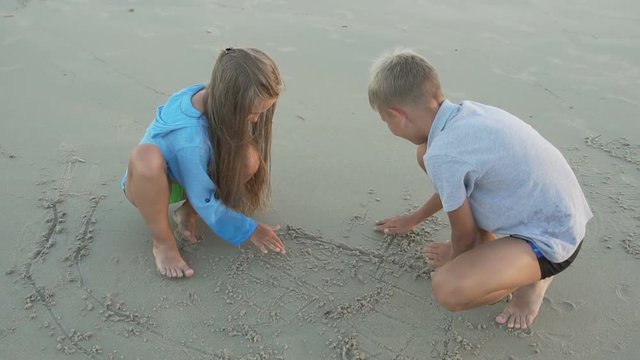 Little sister and brother draw on sand.