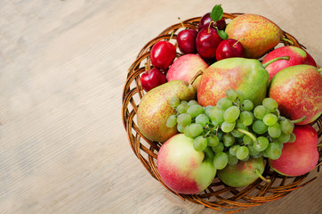 Farm apples, pears, grapes and plums in a wicker wooden plate on the table. Harvest of autumn fruits. Copy Space