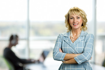 Mature woman with crossed arms. Portrait of cheerful white-skin woman with crossed arms on office background.