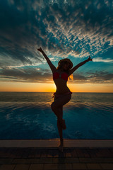 Fototapeta na wymiar Summer Vacation. Silhouette of beauty dancing woman on sunset near the pool with ocean view.