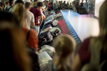 Suitcase on luggage conveyor belt at baggage claim at airport. Lines of people waiting for their...