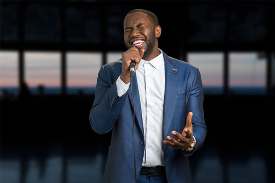 Singing man on the evening background. Darkskinned man with microphone. Black man is singing with closed eyes and passion.
