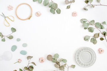 Flat lay border frame with eucalyptus branches, plate and scissors on white background. Top view floral background with space for text.