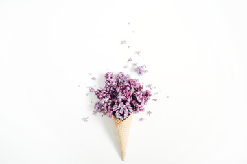 Waffle cone with lilac flower bouquet on white background. Flat lay, top view floral background.
