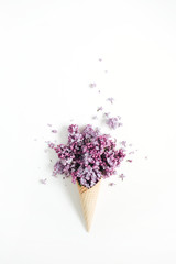 Waffle cone with lilac flower bouquet on white background. Flat lay, top view floral background.