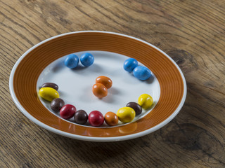 smile from colorfull candy bonbon white brown plate on wooden desk