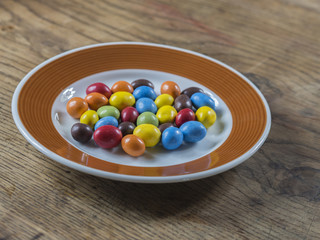 colorful bonbon candy on white brown plate on wooden desk