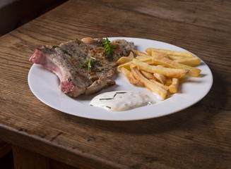 fresh made grilled pork chop steak with french fries chips green herbs nad dressing on white plate on wooden desk