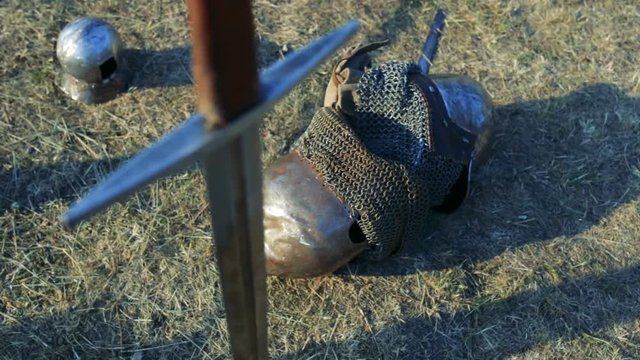 Medieval sword in the ground against the background of armor