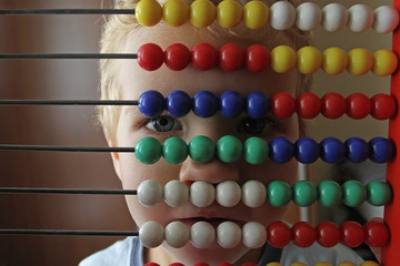 A small toddler boy looks through through the bright bones of wooden accounts. An ancient machine for performing arithmetic operations and a new generation.