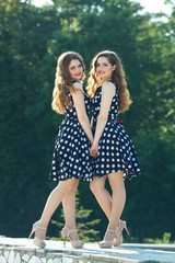 Two beautiful smiling girl sisters twins for a walk in summer park on a background of greenery with makeup and hairstyle