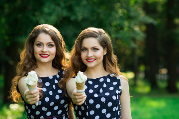 Two girlfriends sister twins of the same appearance with makeup and hairdo in the summer park eating ice cream