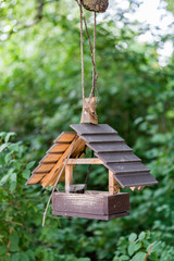 Wooden bird feeder hanging in the green summer park
